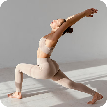 Жінка в бежевому йога-костюмі, освітлена сонцем, з заплющеними очима виконує йога-позу на килимку.